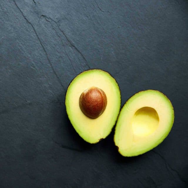 Avocado split in half with pit on a slate background