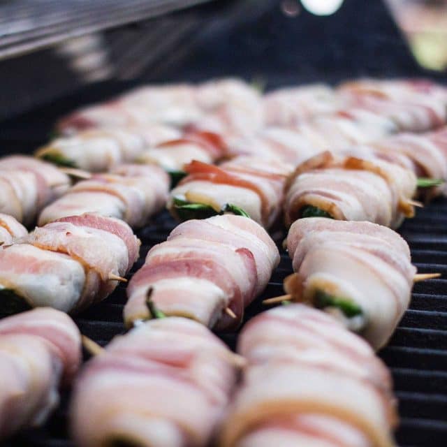 Jalapenos wrapped in bacon on a grill