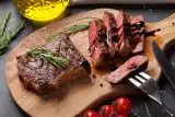 Sliced beef on a wooden board drizzled with balsamic and fresh rosemary