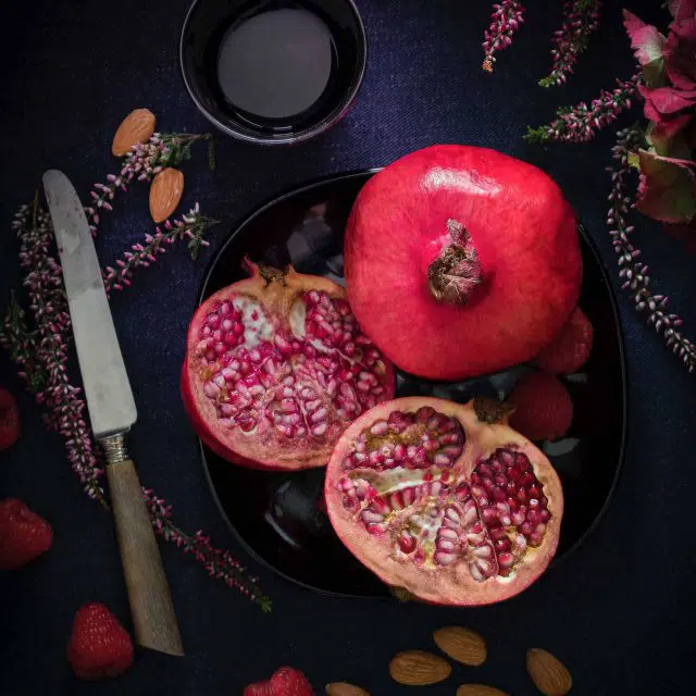 Sliced pomegranate in a bowl next to a small cup of pomegranate balsamic vinegar