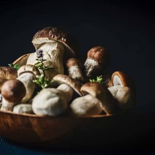 Large wooden bowl full of porcini mushrooms and fresh herbs
