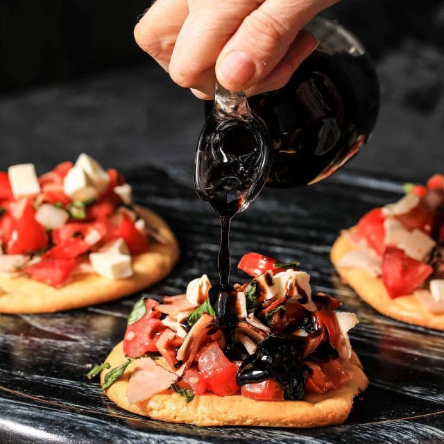 Hand pouring balsamic reduction over appetizers on a platter