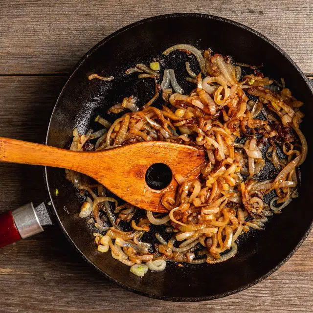 Caramelized onions cooking in a cast iron skillet with a wooden spatula
