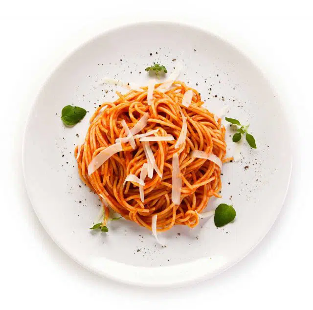 Spaghetti plated on a white plate with fresh herbs and parmesan
