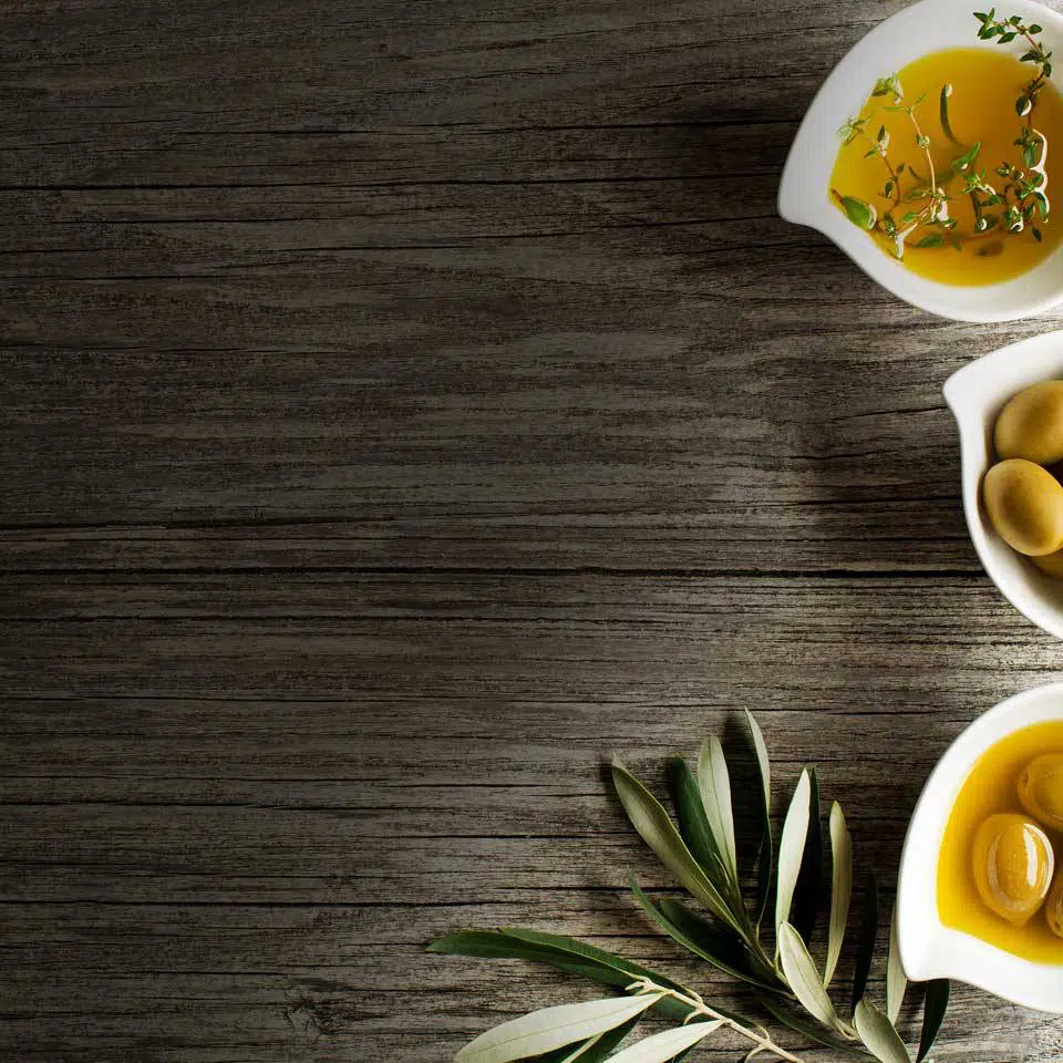 three small bowls full of extra virgin olive oil with herbs on a wooden display board