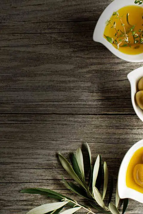 three small bowls full of extra virgin olive oil with herbs on a wooden display board