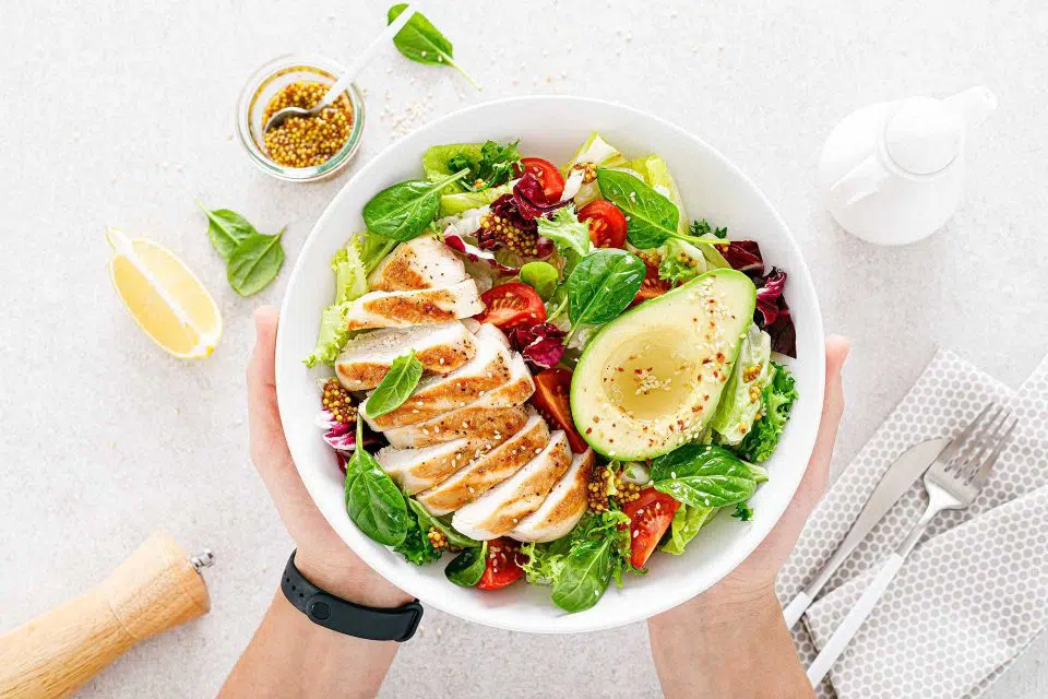 keto diet friendly salad bowl fullk of greens, chicken, tomatoes, avocado, and dressing