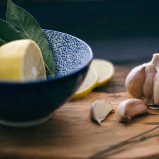 Sliced lemon and bay leaves in a blue bowl next to a bulb of fresh garlic