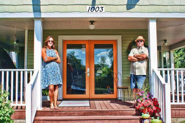 Maria and Billy Hutchison wearing sunglasses with arms folded on the porch of The Olive Branch