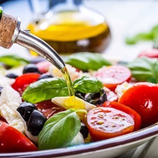 Extra virgin olive oil salad dressing poured over a fresh salad of tomatoes, parmesan chunks, basil, and black olives