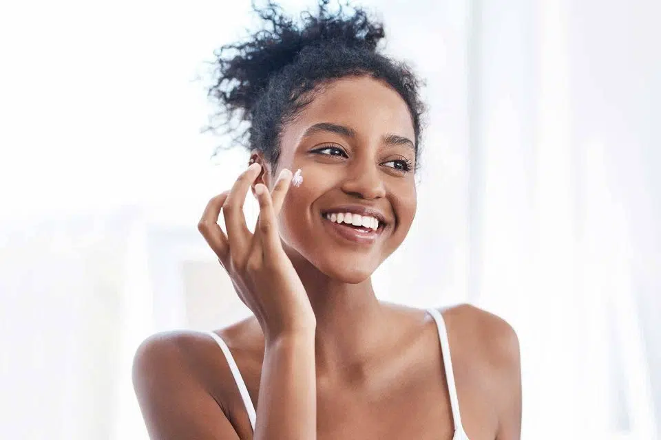 Black woman smiling while using olive oil skincare on her face