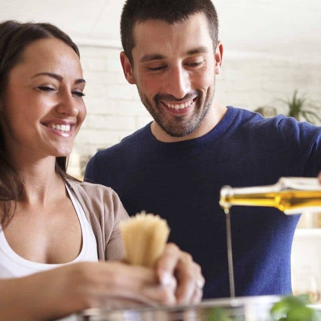 White couple pouring olive oil into a pot and smiling