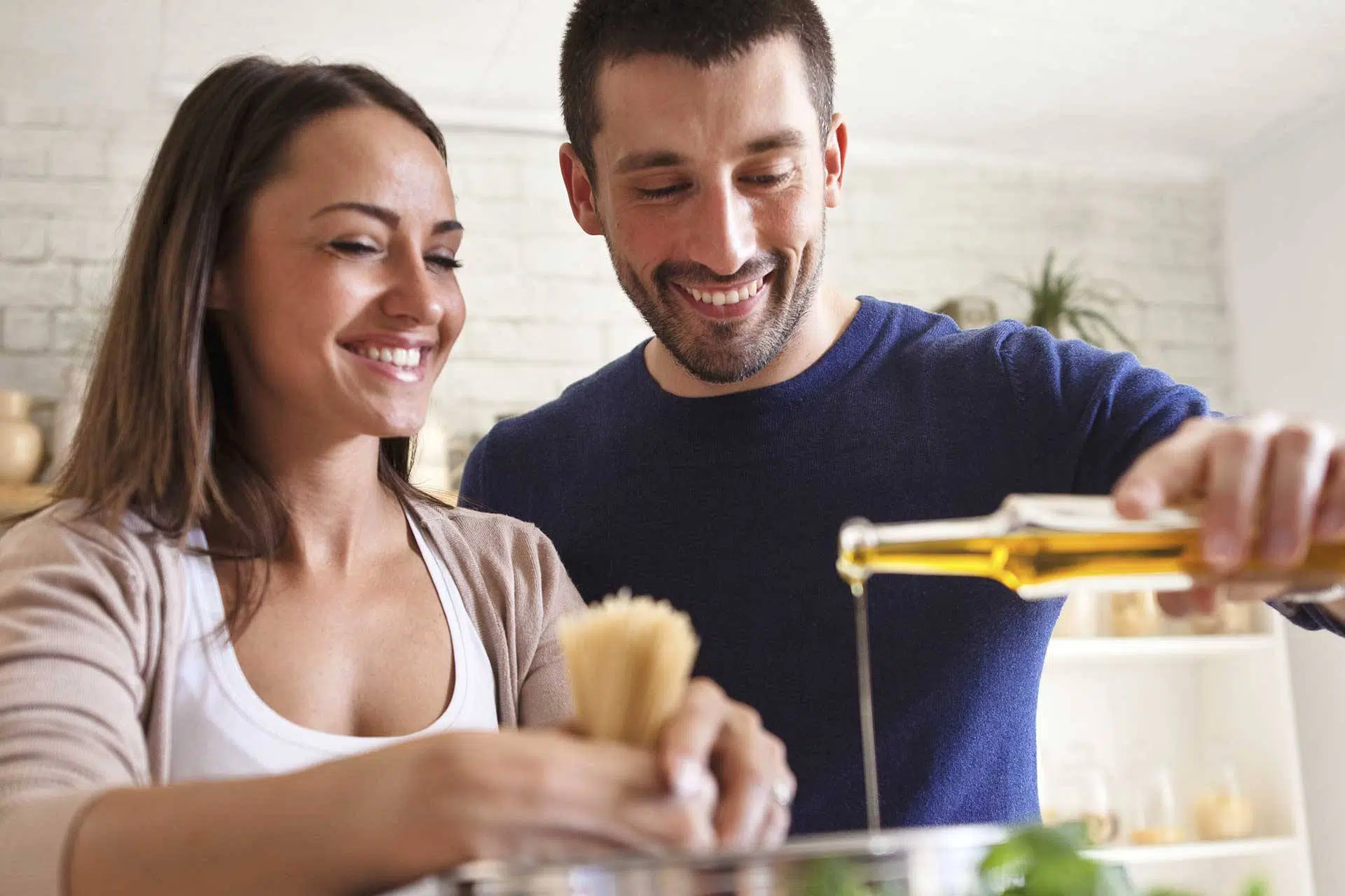 White couple pouring olive oil into a pot and smiling