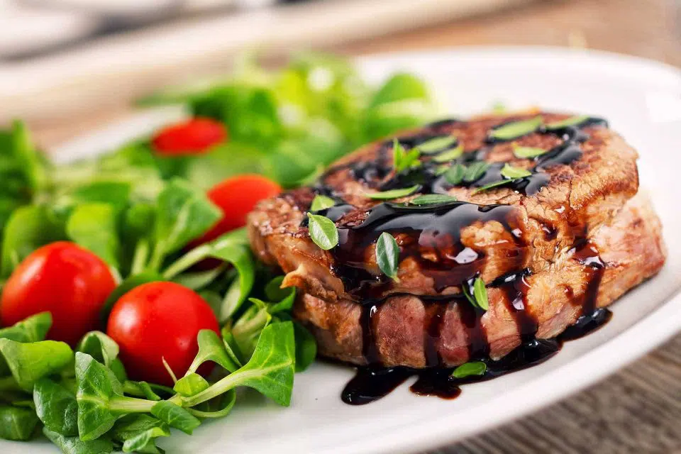 White plate with healthy salad and steak on the side dressed with vinegar and herbs