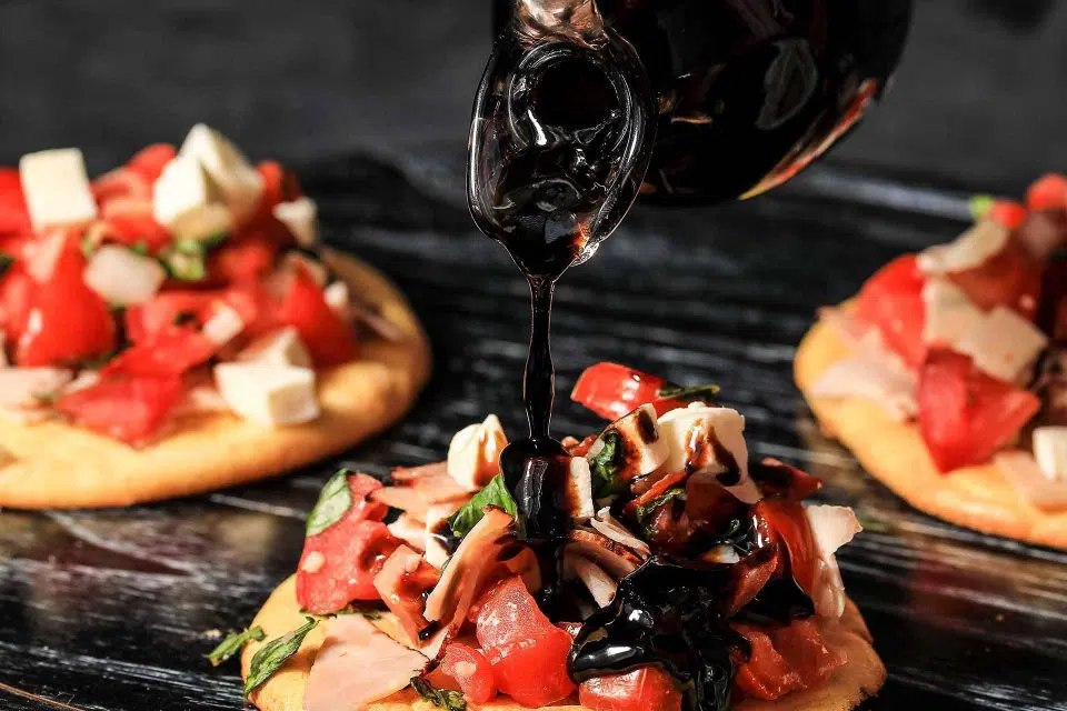 Balsamic reduction being poured onto appetizers
