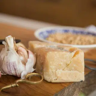 A small brick of parmesan next to a garlic bulb on a wooden board