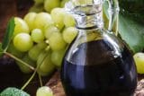 Glass carafe full of wine vinegar next to a cluster of grapes and grape leaves