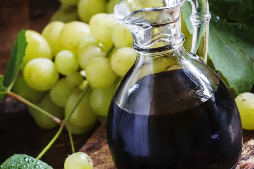 Glass carafe full of wine vinegar next to a cluster of grapes and grape leaves