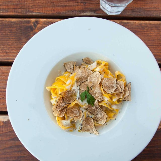 White plate of fresh pasta with white truffles on top